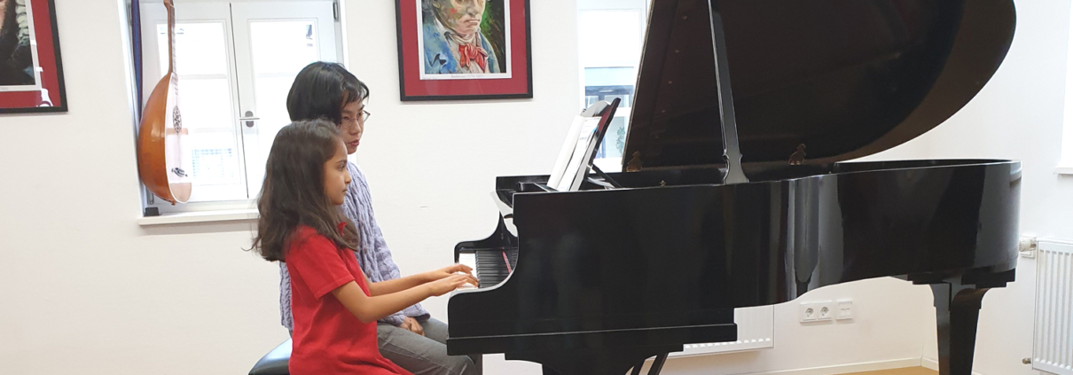 Lehrerin und Schülerin sitzen am Flügel im Flügelsaal der musikkulturschule, der Muskschule im Alten Esel in Lauterbach. Im Hintergrund ein Portrait Ludwig von Beethovens