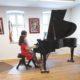 Lehrerin und Schülerin sitzen am Flügel im Flügelsaal der musikkulturschule, der Muskschule im Alten Esel in Lauterbach. Im Hintergrund ein Portrait Ludwig von Beethovens