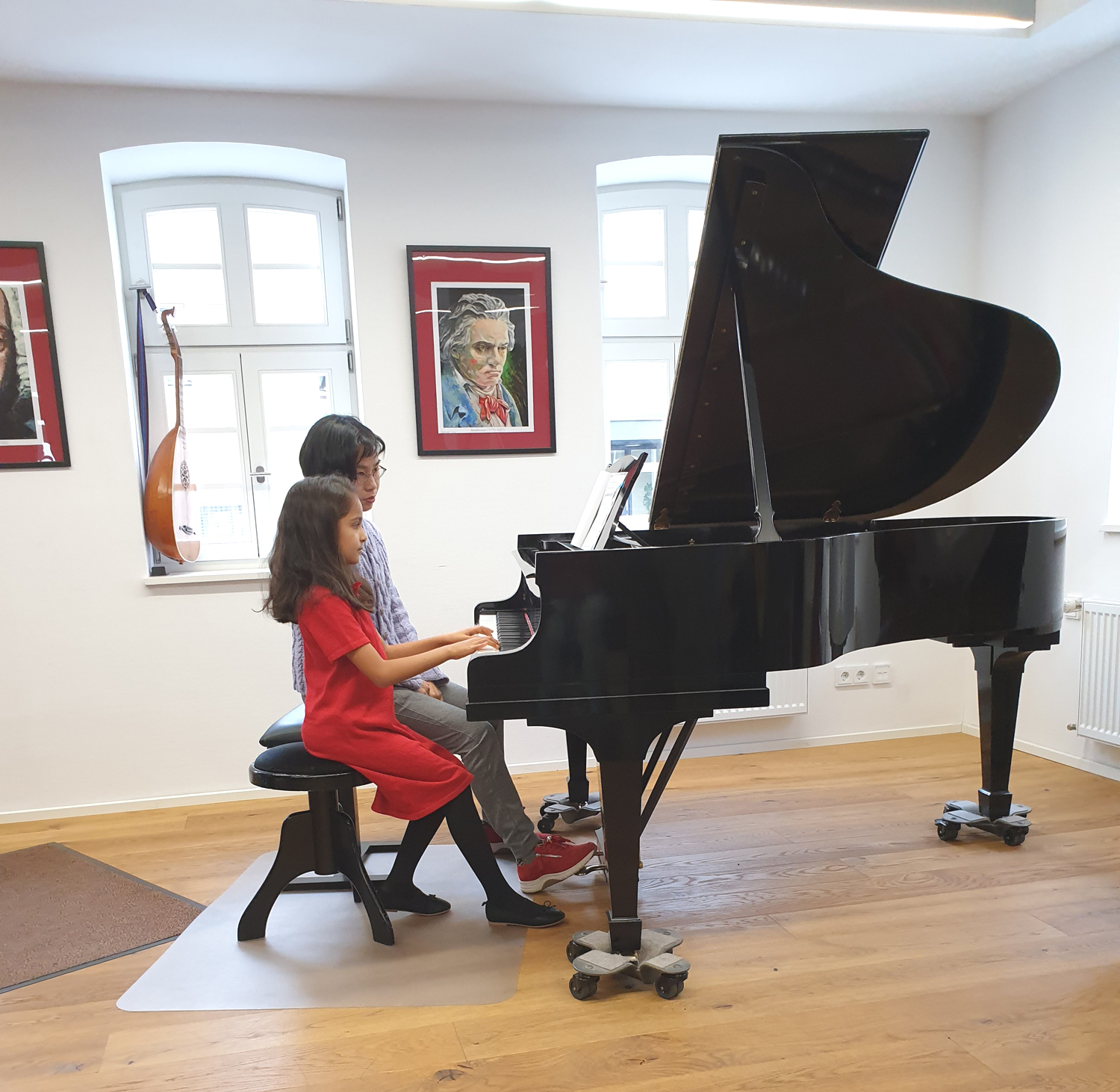 Lehrerin und Schülerin sitzen am Flügel im Flügelsaal der musikkulturschule, der Muskschule im Alten Esel in Lauterbach. Im Hintergrund ein Portrait Ludwig von Beethovens