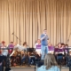 Das Bläserensemble der musikkulturschule Lauterbach und das Bläserensembel aus Niesig sitzen auf der Bühne des Posthotel Johannesberg. Christian Wiegand, Dirigent des Bläserensembles aus Niesig, moderiert.